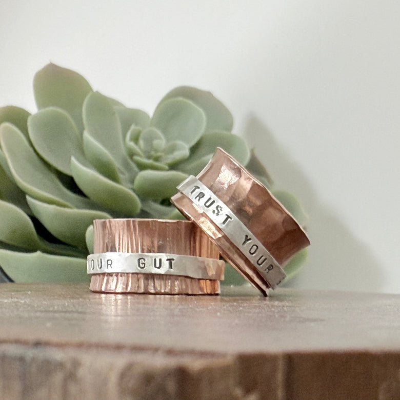 spinner, fidget rings. Two copper rings with engraved text on a wooden surface with a succulent plant in the background.